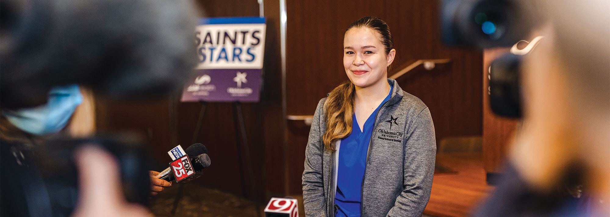 woman smiling in front of news cameras