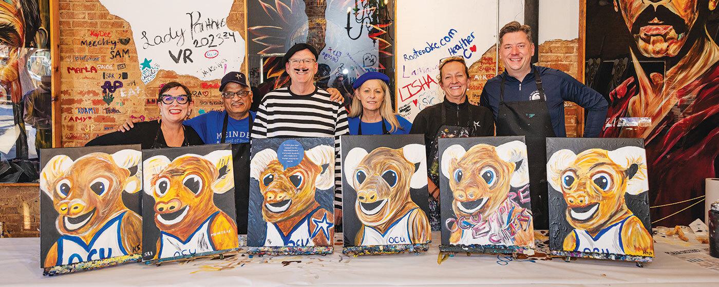 Six people smiling behind painted canvases