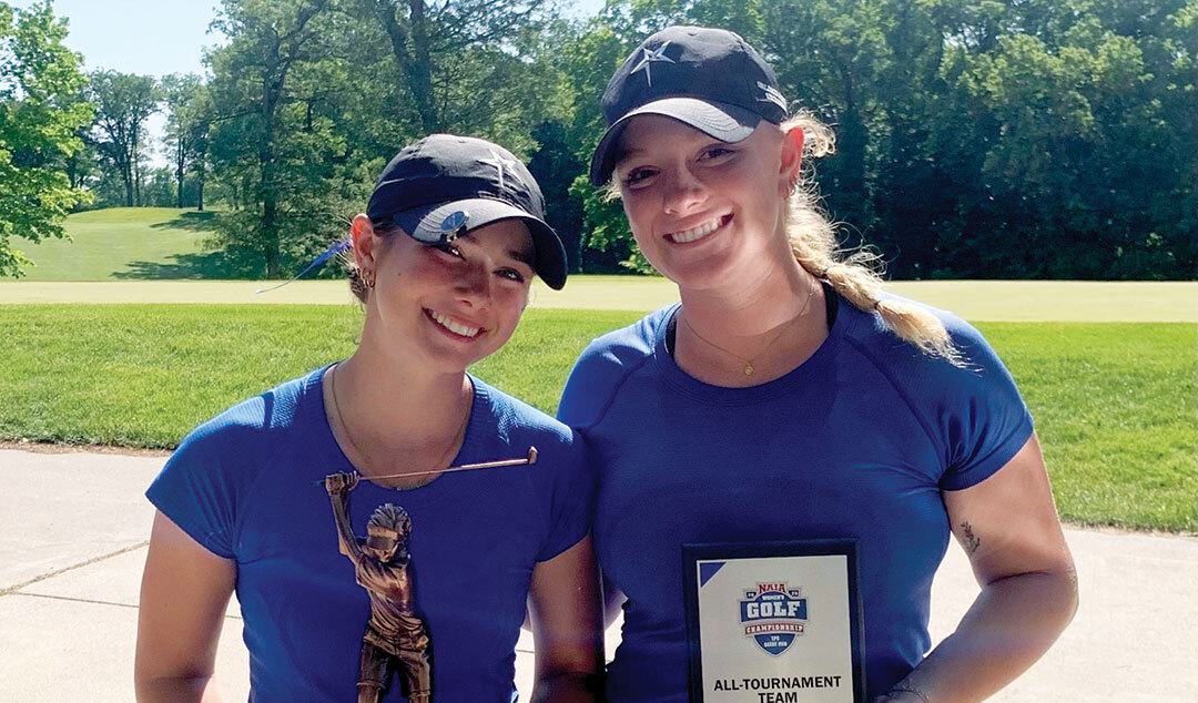 Two women in ball caps holding awards