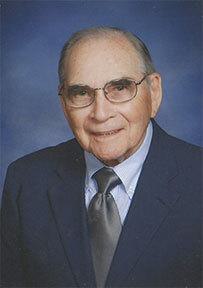 Man in glasses smiling in dark blue suit and tie