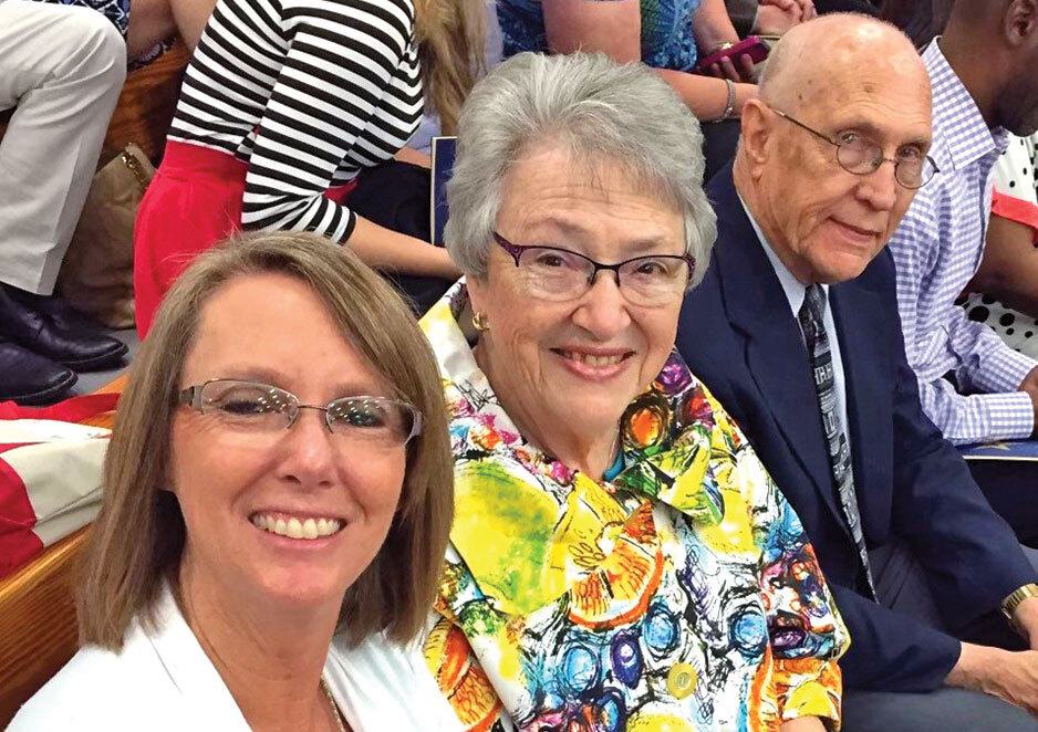 Two women and a man seated in a crowd, all wearing glasses