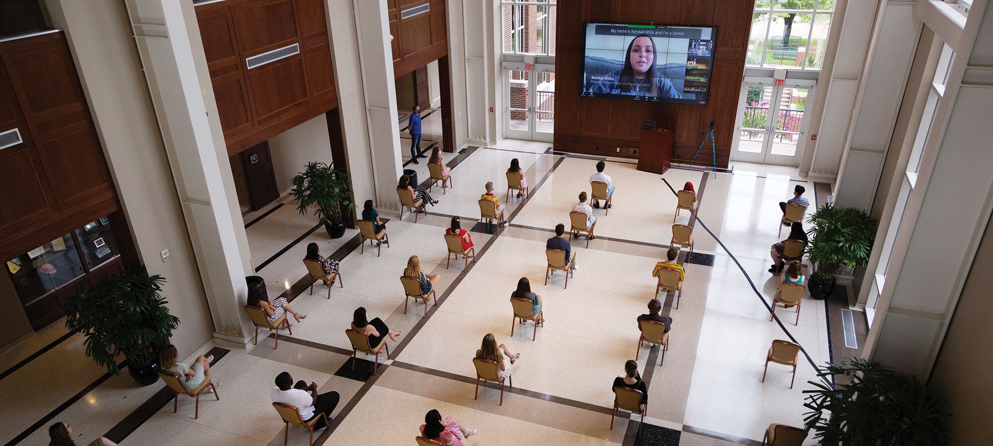 Students seated widely spaced watching digital monitor