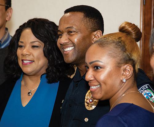 Man in police uniform smiling (Dexter Nelson) surrounded by two smiling women