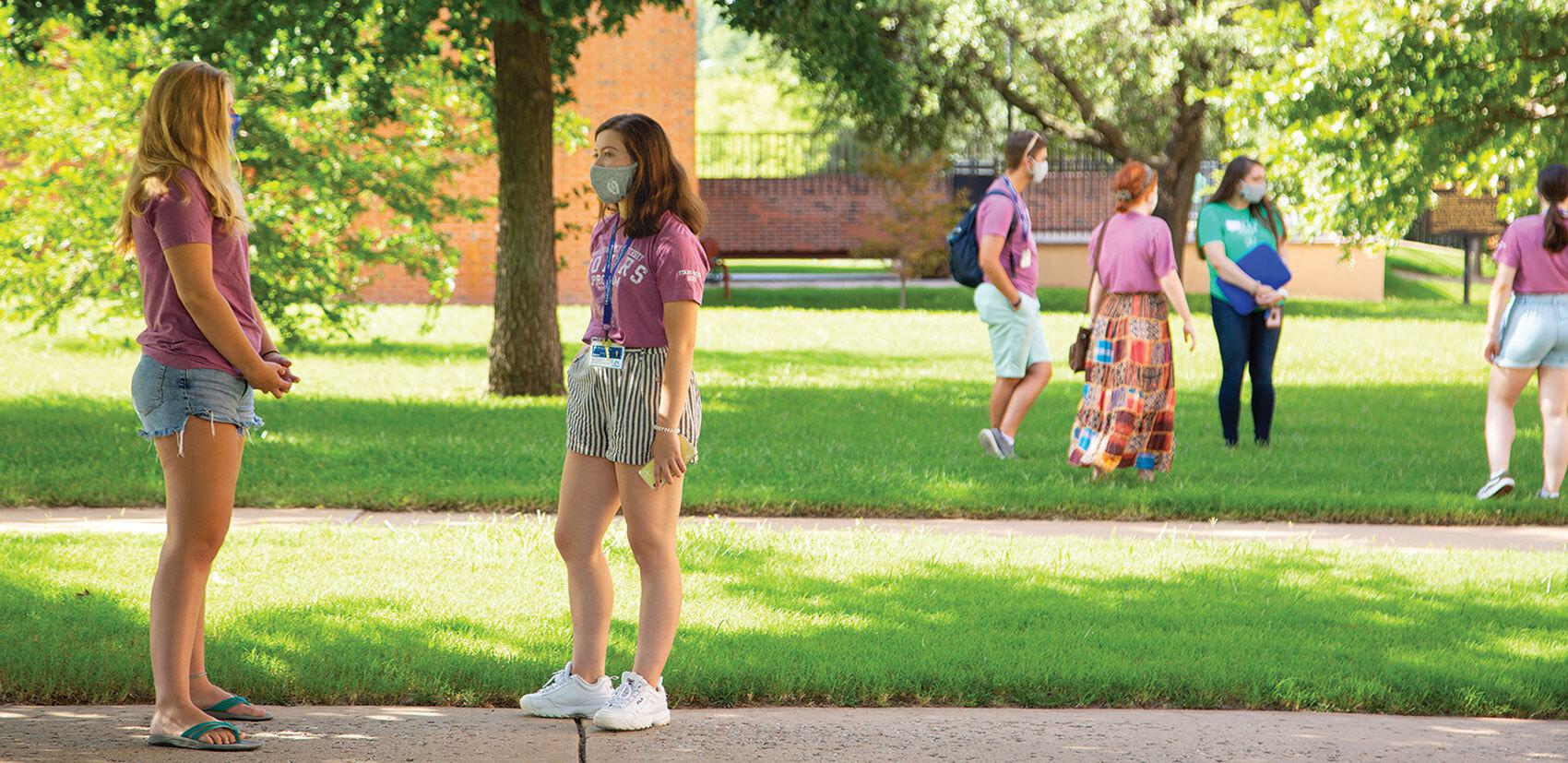 Students standing on grass wearing masks and at a distance